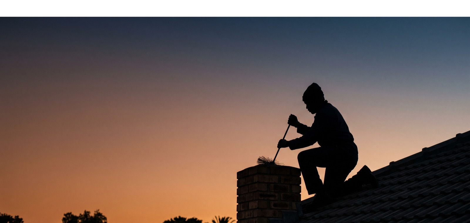 A South African tradesperson silhouetted on a suburban rooftop at golden hour.